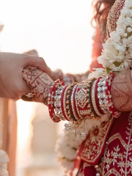A classic wedding shot of the couple holding hands, with a focus on the bride's intricate mehndi and traditional bangles.