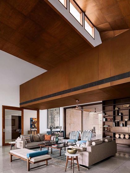 The double-height living room in this Ahmedabad home features a dramatic wooden-clad ceiling and clerestory windows that fill the space with soft, indirect sunlight.