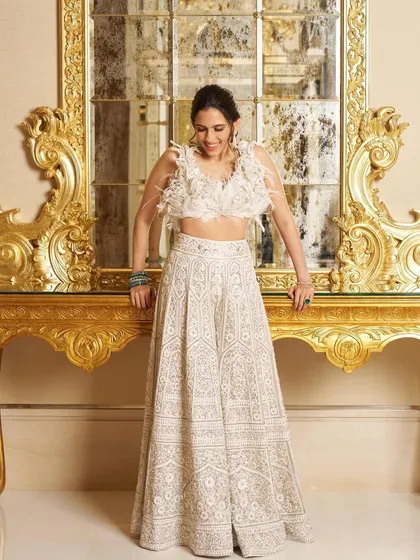 An elegant white lehenga by Manish Malhotra, featuring a feathered blouse and intricate chikankari work on the skirt. It's a chic and modern choice for a Diwali party or reception.