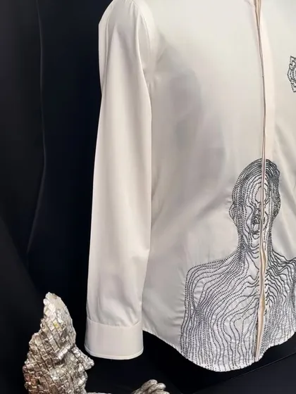 A bold, minimalist white shirt from my latest arrivals. It features an intricate abstract figure embroidered in black thread, merging contemporary art with high fashion.