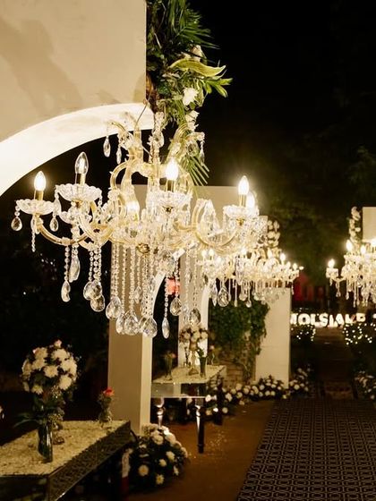 A grand entrance for a glamorous Sangeet, featuring a walkway through white arches adorned with cascading crystal chandeliers and fresh white flowers.