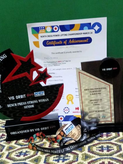 A collection of my trophies, medal, and certificate from the North India Powerlifting Championship. These are symbols of dedication.