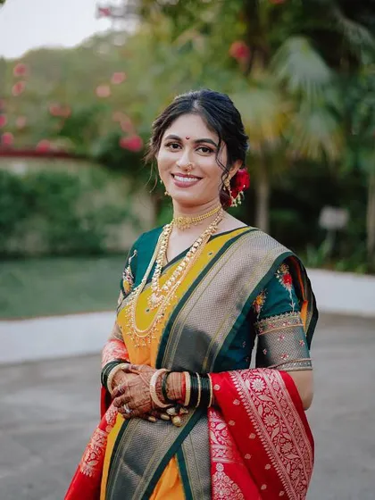 A happy bride in her Nauvari saree. The makeup is fresh and radiant, with a simple hair updo adorned with flowers, perfect for a traditional Maharashtrian wedding.