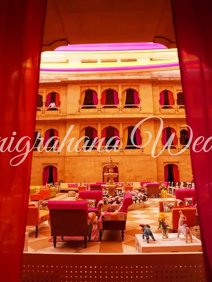 A dramatic view of the colorful Mehendi setup through a red curtain, creating a sense of anticipation.