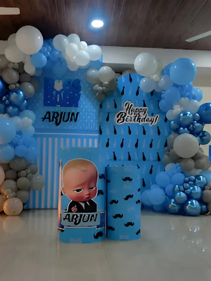 A fun Boss Baby theme for a first birthday celebration. The decor uses a blue and white color scheme with custom backdrops, character cutouts, themed pedestals, and a large light-up number '1'.