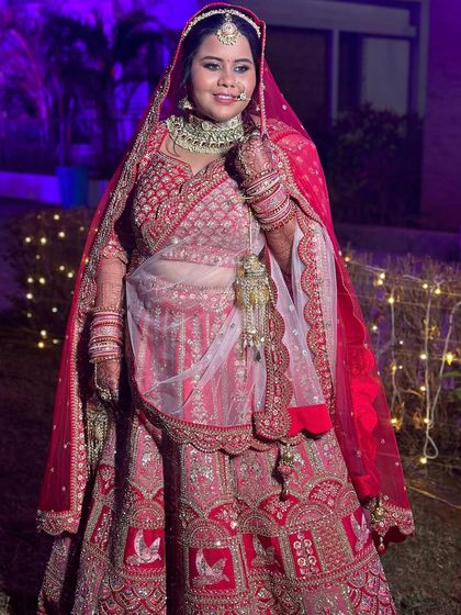 The full view of the bride's stunning red and white lehenga. The makeup is designed to complement the intricate embroidery and colors of her outfit.