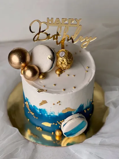 A stylish and masculine design perfect for him. This rich vanilla buttercream cake features a blue watercolor effect, gold leaf, macarons, and a Ferrero Rocher topper.