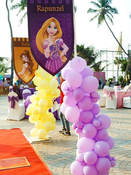 A Rapunzel-themed banner and colorful balloon columns line the entrance walkway.