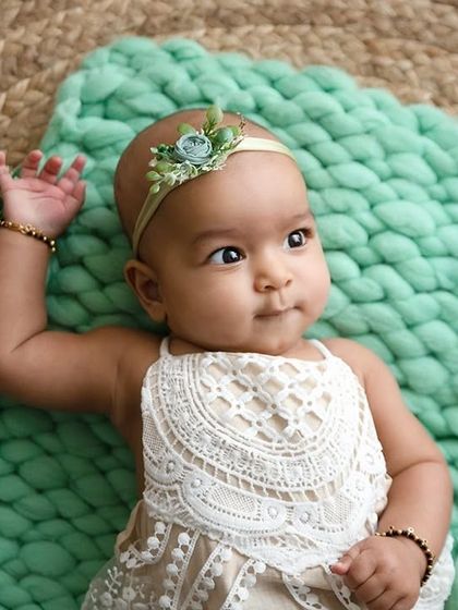A baby girl in a lace outfit lies on a soft green blanket, looking to the side.
