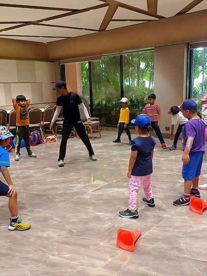 A coach leads a group of young children in a fun, active game. Our sessions for the little ones are designed to be engaging and playful, fostering a positive association with fitness.