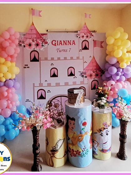 A Beauty and the Beast-themed seventh birthday. The setup includes a castle backdrop, character-printed plinths, and colorful balloon columns.