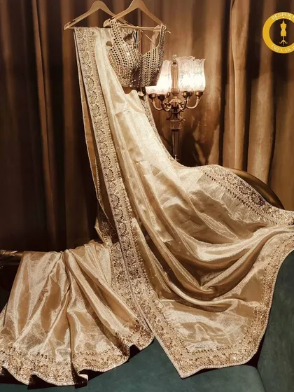 Six yards of pure magic. This golden tissue saree with a detailed border and matching blouse is the epitome of traditional luxury.
