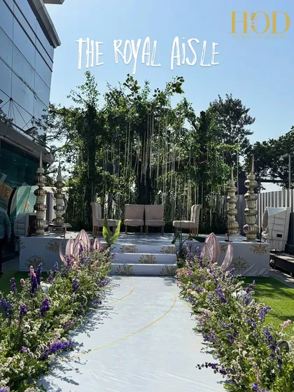 The "Royal Aisle" leading to the Varmala stage, lined with purple and white flowers, creating a majestic path for the couple.