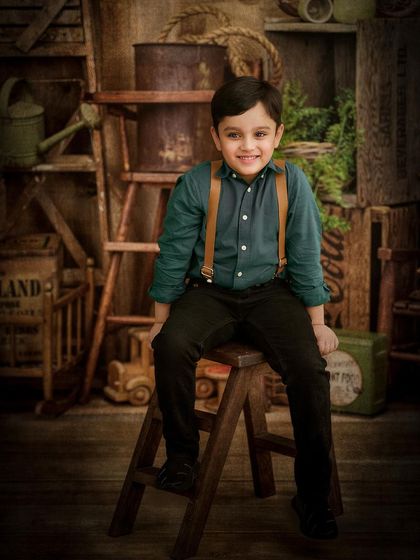 A happy young boy poses in our rustic "Wood Shed" studio set. The suspenders and dark-toned outfit complement the vintage, barn-like feel of the backdrop.
