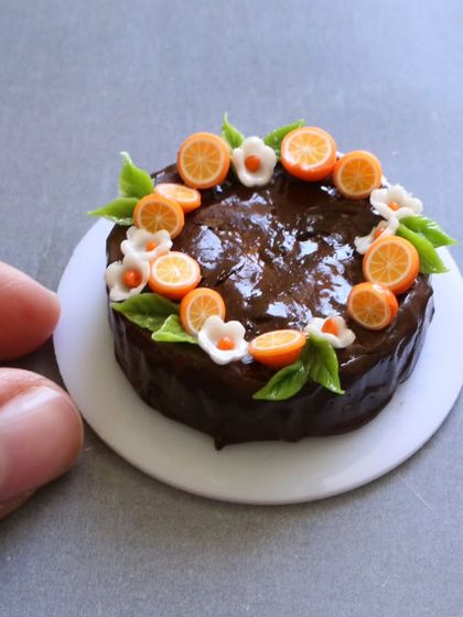 A close-up of a miniature chocolate fruit cake, decorated with tiny orange slices.