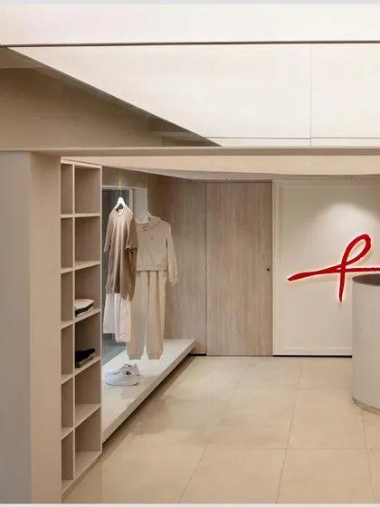 The store layout is designed to be open and uncluttered, with integrated shelving and display areas. The neutral color palette allows the merchandise to stand out, while the red brand logo provides a strong visual anchor.