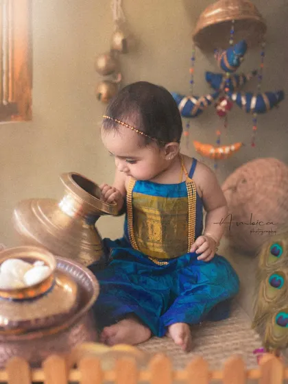 Our little Radha, styled in a beautiful blue and gold outfit, explores a pot of "butter" in a scene inspired by the rustic homes of Vrindavan.