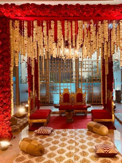 For a royal and traditional wedding theme, I designed this stunning indoor mandap. The entire structure is draped in rich red florals, with hanging floral strings and a small chandelier, complemented by regal seating for the bride and groom.