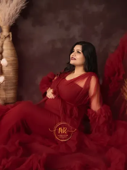 A luxurious seated portrait in a deep red ruffled gown. The rich color and texture of the dress create a feeling of opulence, complemented by the rustic studio decor.