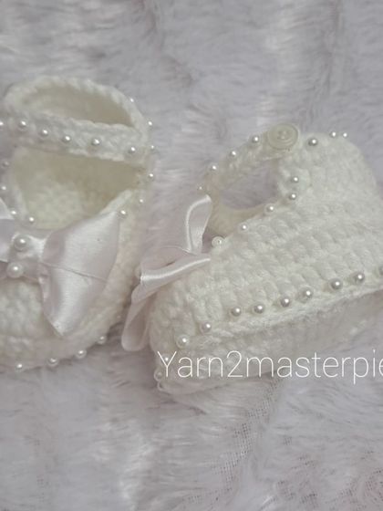 These white booties are perfect for a formal occasion, featuring a delicate strap adorned with pearls and a large, soft satin bow on the front.