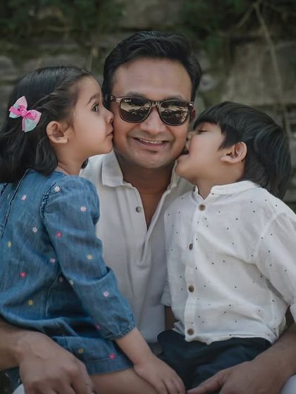 A father receives affectionate kisses from his son and daughter in a heartwarming outdoor portrait.