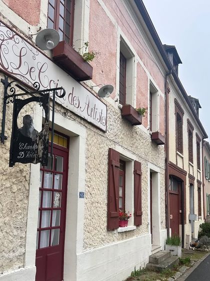 The facade of "Le Secret des Artistes" in a quaint European town. The textured walls, rustic shutters, and charming signage are the kinds of thoughtful details that add character and tell a story.