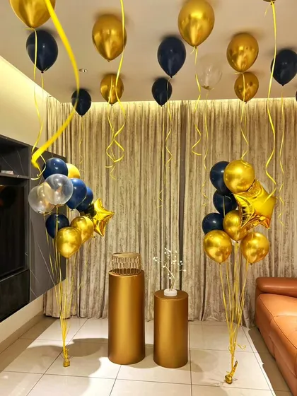 A simple yet elegant indoor birthday decoration. This setup uses gold and navy blue balloon bouquets, including star-shaped foils, and golden pedestals to create a sophisticated party corner in any room.