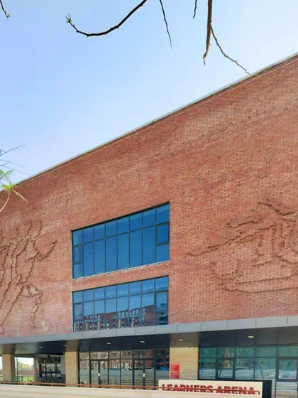 The "Learners Arena" at Rishihood University features a striking brick facade with intricate murals. This building serves as a landmark on campus, representing the institution's commitment to both artistic expression and academic pursuit.