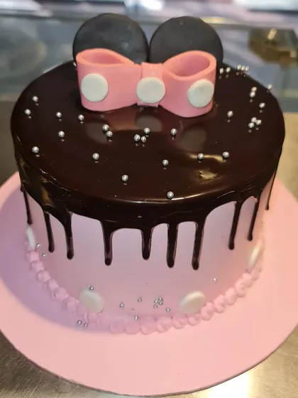 A chic and simple Minnie Mouse drip cake. The combination of pink frosting, a rich chocolate drip, and Minnie's iconic bow and ears makes for a stylish and delicious birthday treat.
