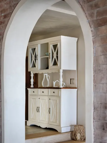 A view through an archway reveals a custom-designed white crockery unit. This piece blends classic farmhouse style with the villa's overall rustic charm.