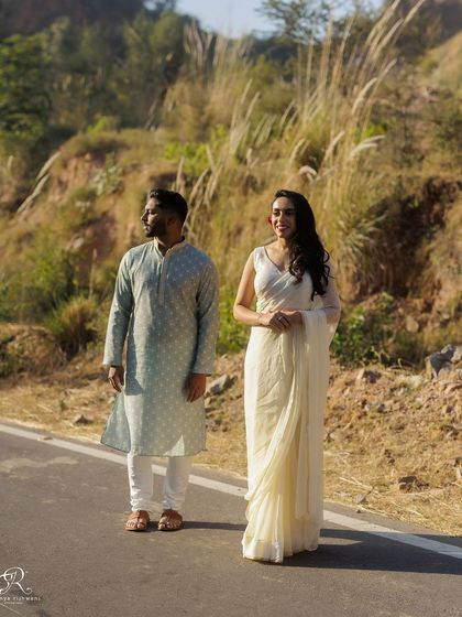 A classic, poised shot of the couple standing on the road. It showcases their beautiful traditional attire and the serene landscape of their outdoor photoshoot location near Delhi.