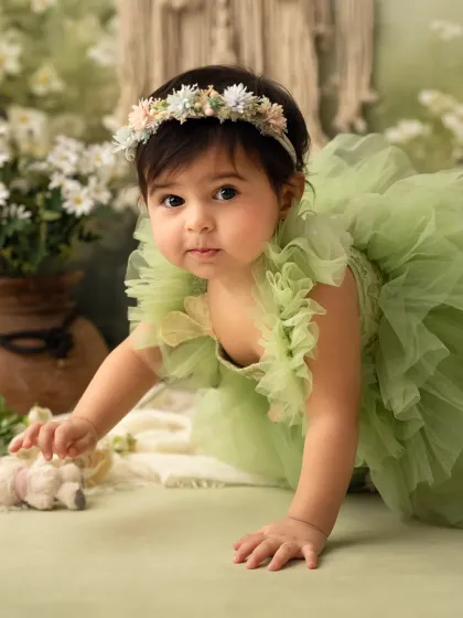 A baby girl in a green dress crawls through a field of studio flowers. This is a beautiful setup for a sitter session.