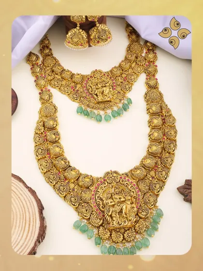 This magnificent double-layered temple jewellery set is a masterpiece of our heritage collection. Crafted in antique-finish 22kt gold with green bead accents, it features detailed carvings of Lord Krishna, making it a highly sought-after piece for discerning bridal customers.