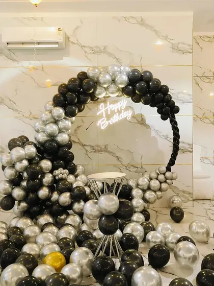 A chic and modern birthday setup with a black and silver balloon ring. The 'Happy Birthday' neon sign adds a cool touch, making it perfect for an adult's birthday party.