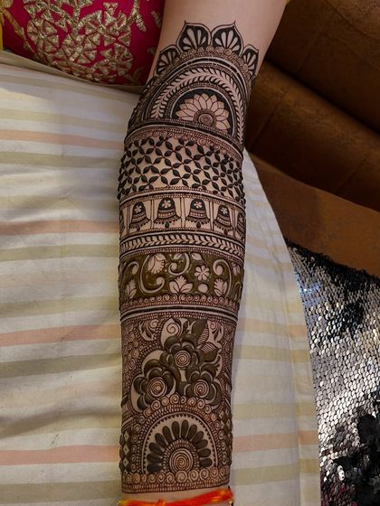 This full arm mehandi is packed with traditional elements. You can see temple bells (ghanti), floral patterns, and geometric checks, creating a rich and dense design.