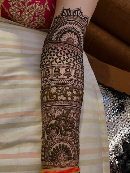 This arm design features hanging temple bells (jhumkas) and various intricate filler patterns, covering the arm from wrist to elbow.