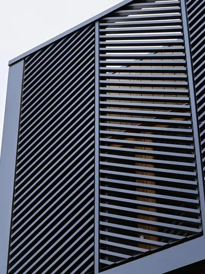 A close-up view of a building facade featuring louvered metal panels set at an angle. This architectural detail adds texture and a modern aesthetic while providing privacy and controlling sunlight.