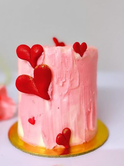 This pink mini cake is decorated with a textured buttercream finish and adorned with handcrafted red hearts, making it a simple yet heartfelt romantic gesture.