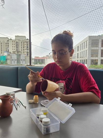 A young participant is deep in concentration as she paints her terracotta pot on the rooftop terrace, with the city view behind her.