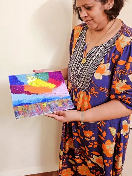 A student proudly holding her finished "Expressive Sky" painting, created during a palette knife workshop at our studio.