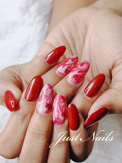 A full view of the striking red and white marble nail art on long, almond-shaped extensions.