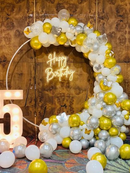 A beautiful 5th birthday setup with a white ring backdrop, a cascade of gold, white, and silver balloons, and a large light-up number '5'.
