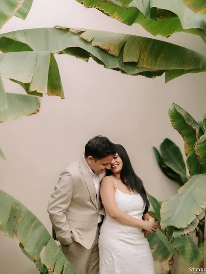 A sweet and romantic embrace, framed by lush green leaves, showcasing the couple's gentle connection.
