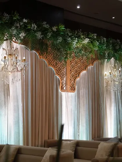 The full lounge backdrop, showing the combination of hanging greenery, chandeliers, and traditional jali arches, creating a rich and textured design.