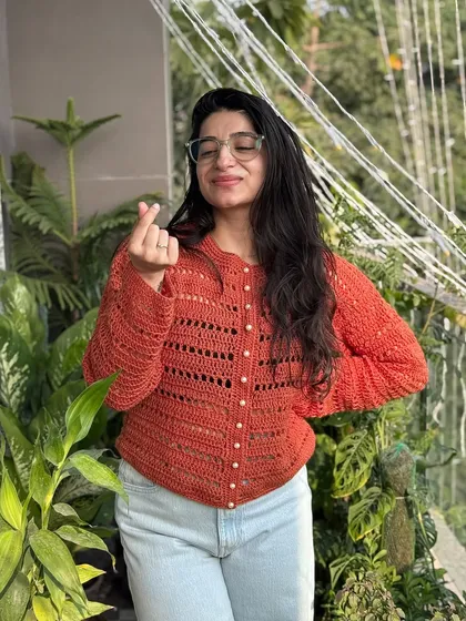 This beautiful rust-colored cardigan features delicate openwork stitching and pearl-like buttons. It's a lightweight yet warm piece that can be dressed up or down, making it a versatile addition to your wardrobe.
