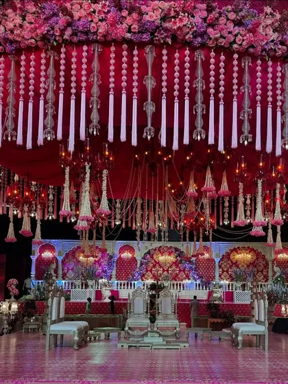 A magnificent, circular mandap structure with a canopy of red fabric and thousands of hanging floral tassels and crystals. This design creates a dramatic and opulent focal point in the center of the grand hall.