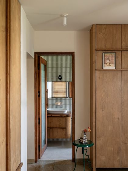A view from the hallway into one of the bathrooms, showcasing the consistent material palette. The warmth of the teak wood door contrasts beautifully with the cool, simple tiles inside.