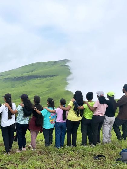A group of friends with their arms around each other, looking at the iconic "sea of clouds" at Nethravathi peak.