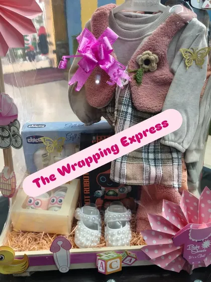 The final look of the baby girl hamper, complete with a cute dress, shoes, and toys, all wrapped up with a pink bow.