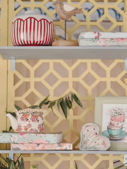 A styled shelf with a bird statue, a striped vase, and other whimsical props against a yellow jaali screen.